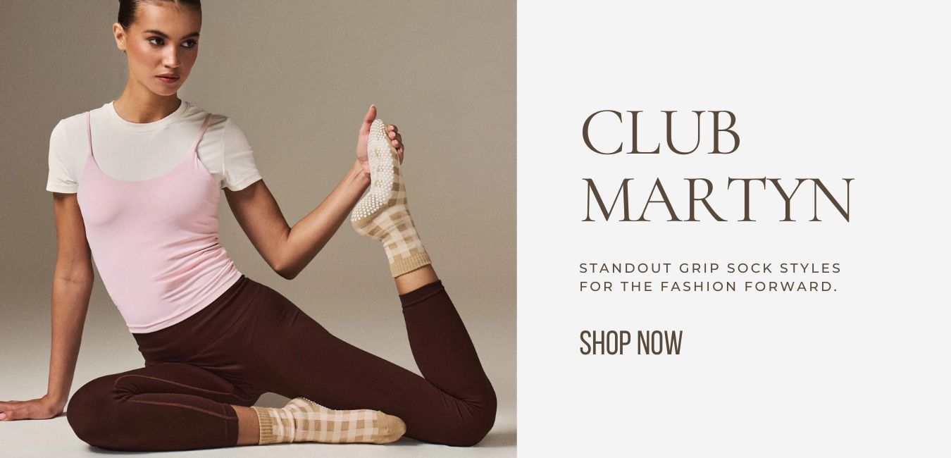 Woman sitting on the floor wearing a white and pink top and brown pants with beige socks, promoting Club Martyn sock styles.