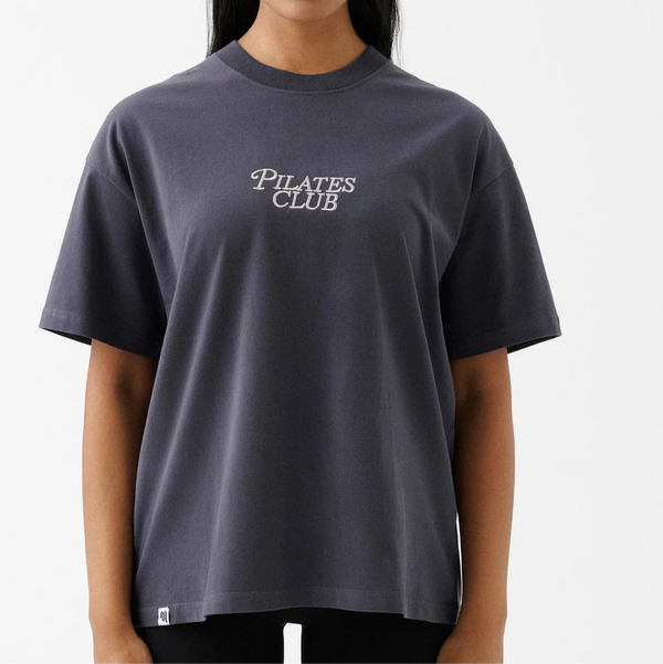 Woman wearing a dark gray t-shirt with 'Pilates Club' text on a white background