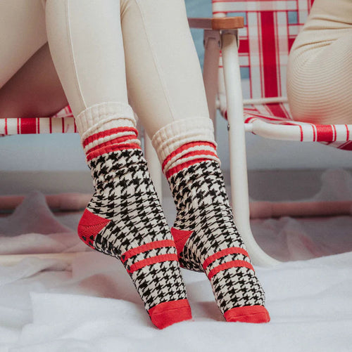 Person wearing houndstooth pattern socks with red accents on a beach chair.
