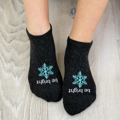 Black socks with blue snowflakes and white text on a wooden floor.