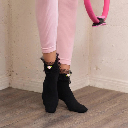 Person wearing pink leggings and black ankle boots holding a pink hoop against a white brick wall.