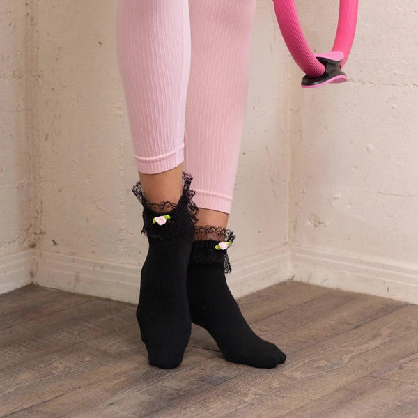 Person wearing pink leggings and black ankle boots holding a pink hoop against a white brick wall.