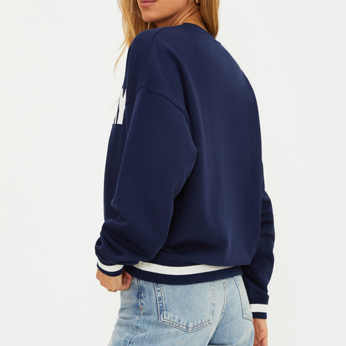 Woman wearing a navy blue sweatshirt with white text and light blue jeans on a white background