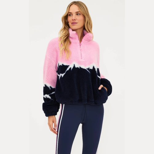 Woman wearing a pink and navy print pullover with navy pants on a white background