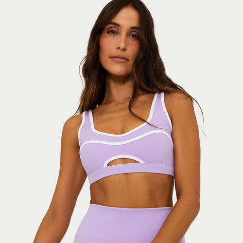 Woman wearing a light purple sports bra and leggings on a plain background