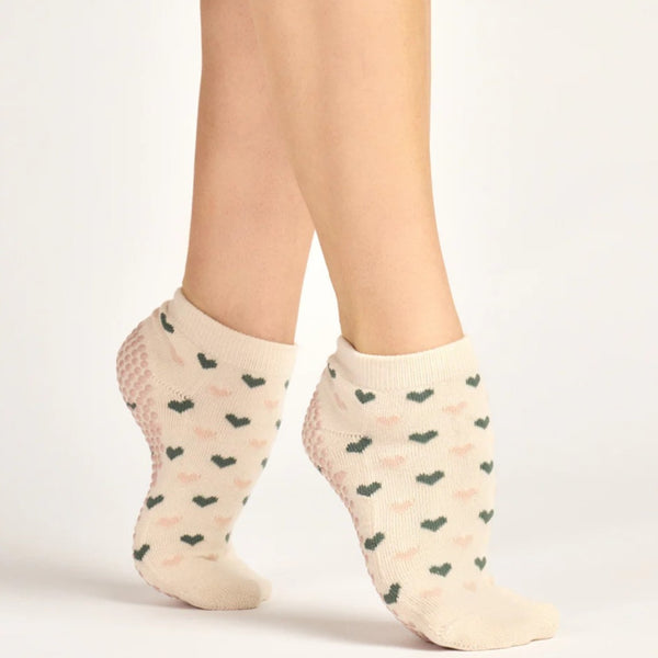 Beige ankle socks with black heart patterns worn by a person on a white background