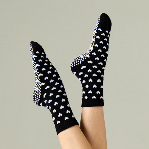 Black socks with white heart patterns worn by a person on a neutral background