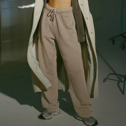 Person wearing a long coat over a sports bra and jogger pants in an indoor setting
