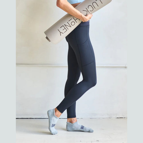 Person wearing dark gray leggings holding a yoga mat with 'Lucky Honey' branding.