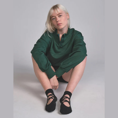 Woman wearing a green sweater and black shoes on a gray background