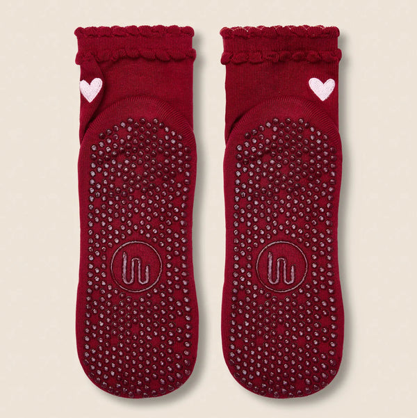 Pair of red socks with textured sole and heart design on a beige background