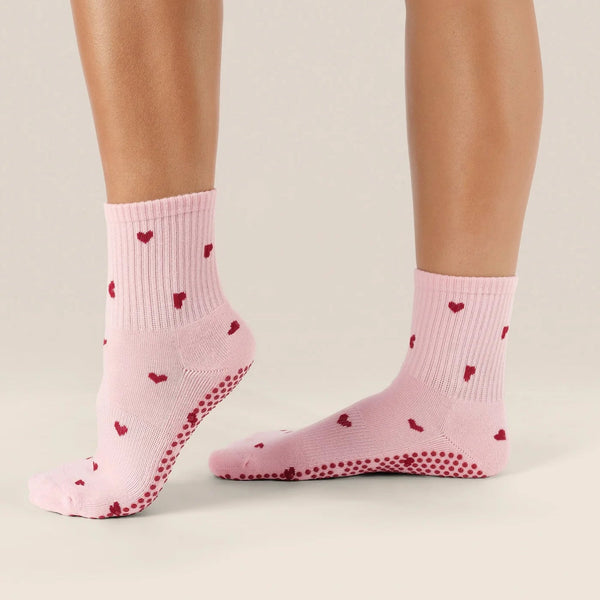 Pink socks with red heart patterns worn by a person on a neutral background