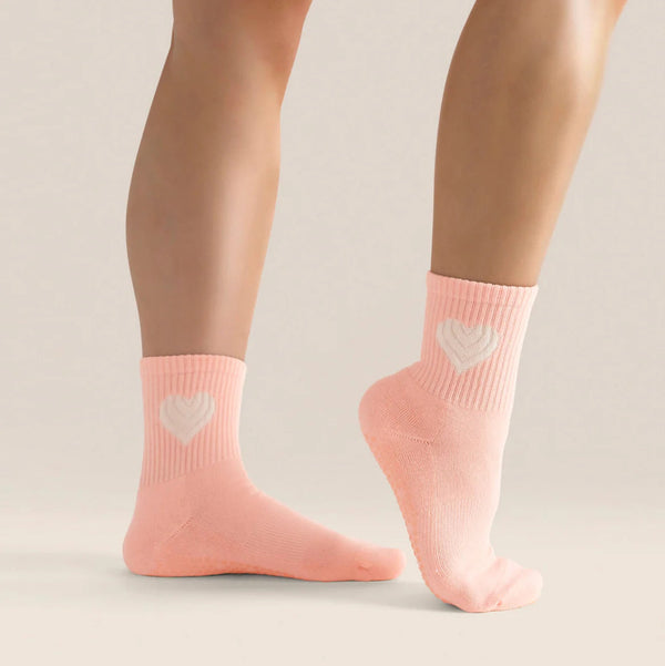 Pink socks with heart designs worn by a person on a neutral background