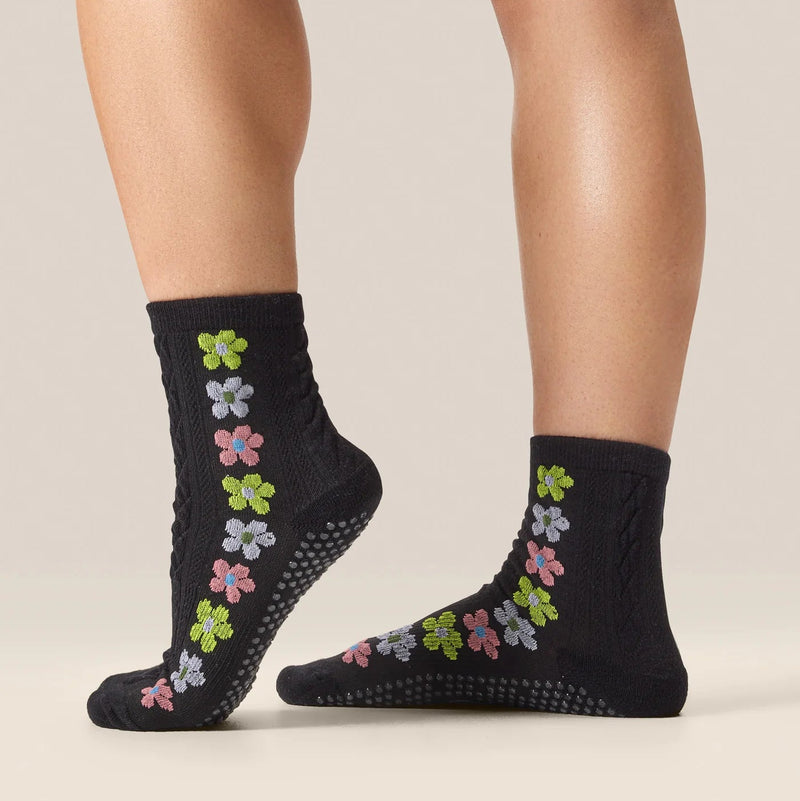 Black socks with colorful flower patterns worn by a person on a neutral background