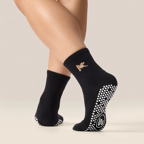 Black socks with grip dots worn by a person on a beige background