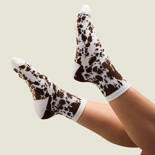 Cow print socks worn by a person on a plain background