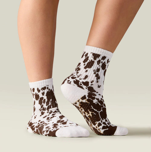 Cow print socks worn by a person on a neutral background
