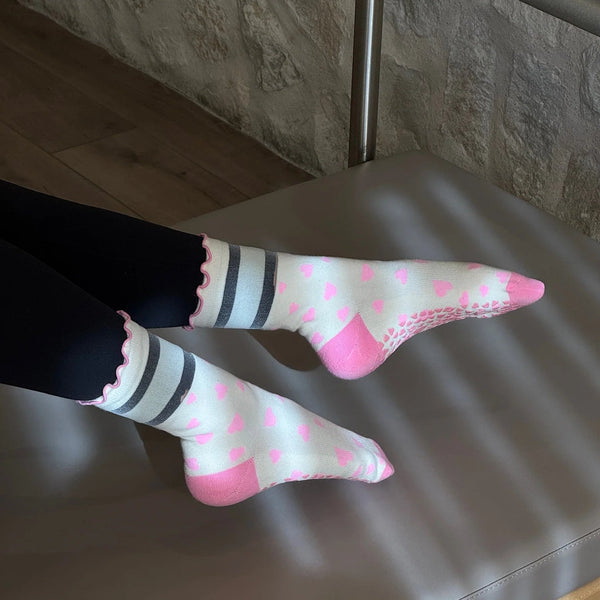 Person wearing pink socks with white polka dots and black stripes on a gray surface.