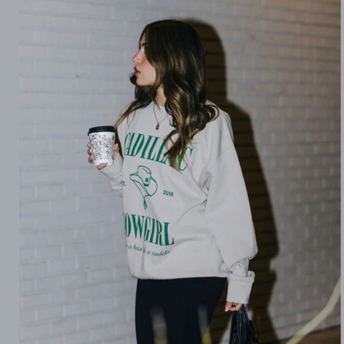 Woman wearing a sweatshirt with text and graphics, holding a cup against a brick wall.