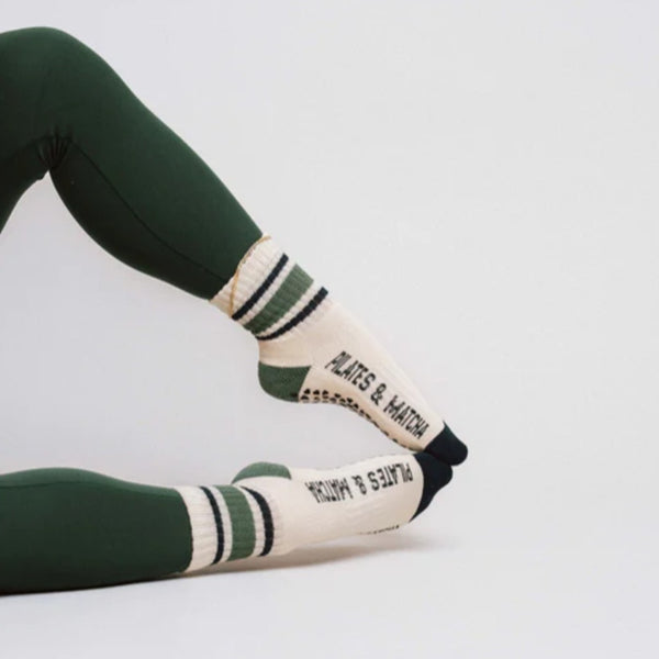 Person wearing green leggings and white socks with black and green stripes on a light gray background