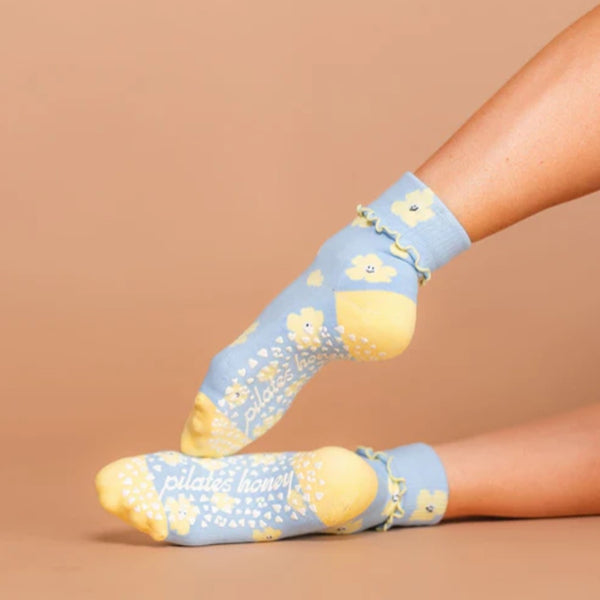 Light blue socks with yellow lemon designs and 'pilates honey' text on a beige background
