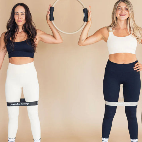 Two women in athletic wear holding exercise hoops against a beige background