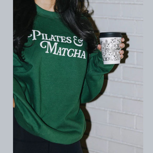 Person wearing a green sweatshirt with 'Pilates & Matcha' text, holding a coffee cup.