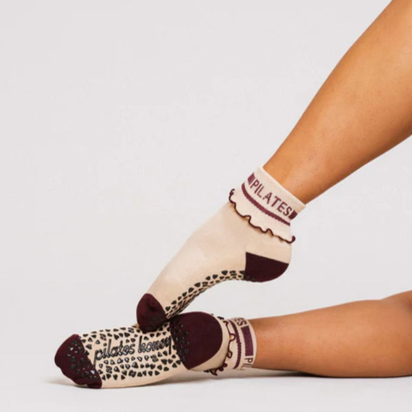 Beige socks with brown accents and 'Pilates' text on a light gray background