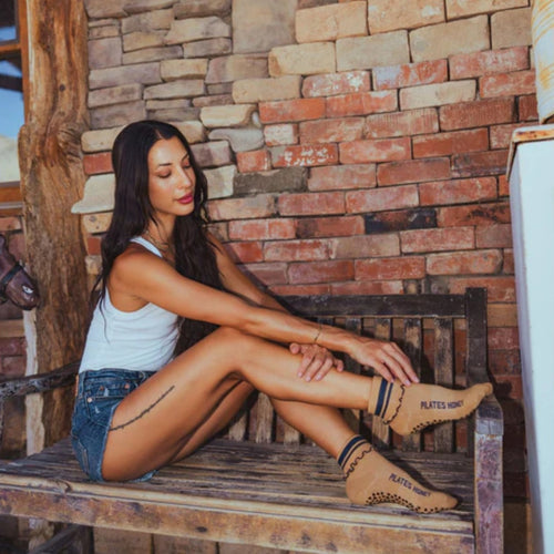 Woman sitting on a wooden bench wearing brown boots with text, against a brick wall.