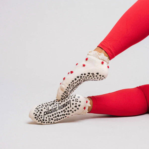 White socks with red rosettes worn by a person in red leggings on a light gray background