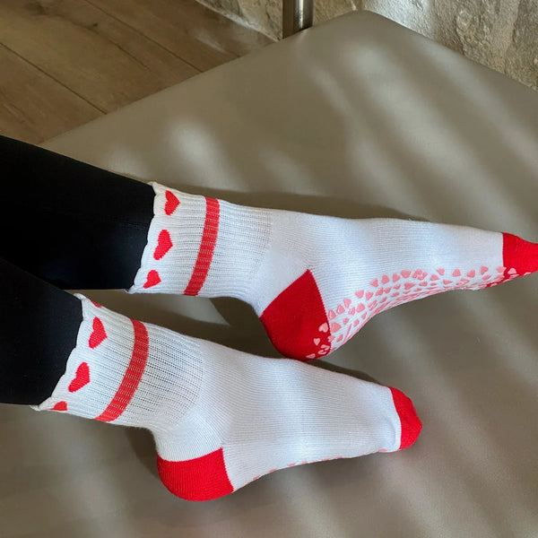 Person wearing black leggings and white socks with red hearts on a wooden floor.