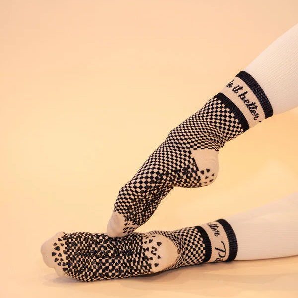 Person wearing black and white patterned socks with visible branding on a beige background