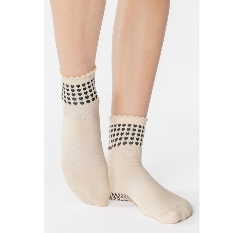 Beige socks with black heart patterns worn by a person on a white background