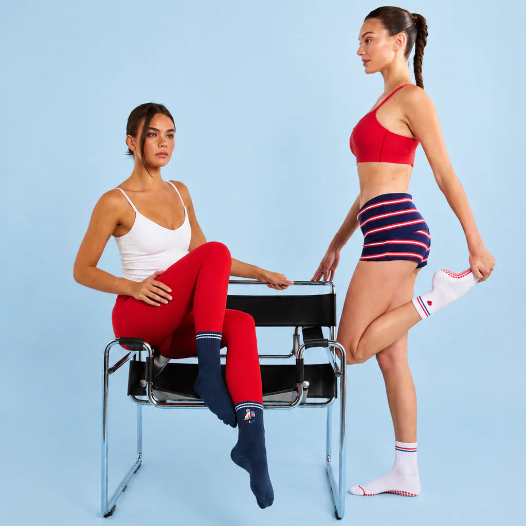 Two women in athletic wear posing on a chair against a blue background
