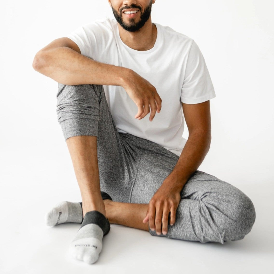 Man sitting on a white floor wearing a white t-shirt and gray pants.