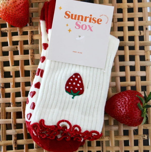 White sock with red accents and strawberry design on a woven surface with strawberries.