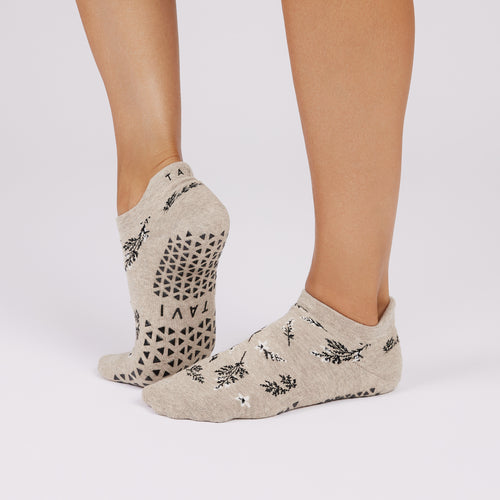 Beige ankle socks with black patterns worn by a person on a light gray background
