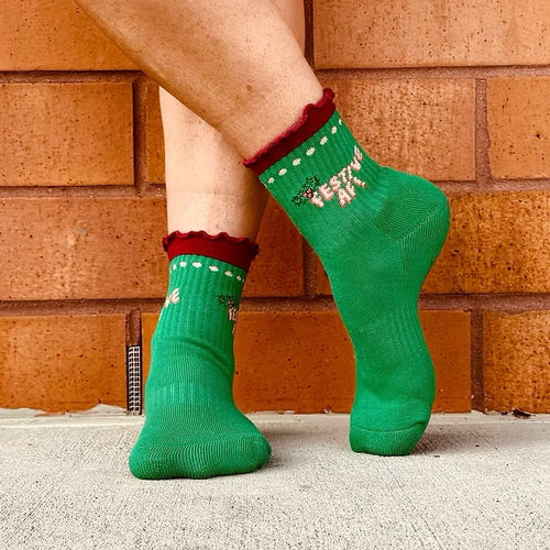 Green socks with red trim worn by a person against a brick wall.