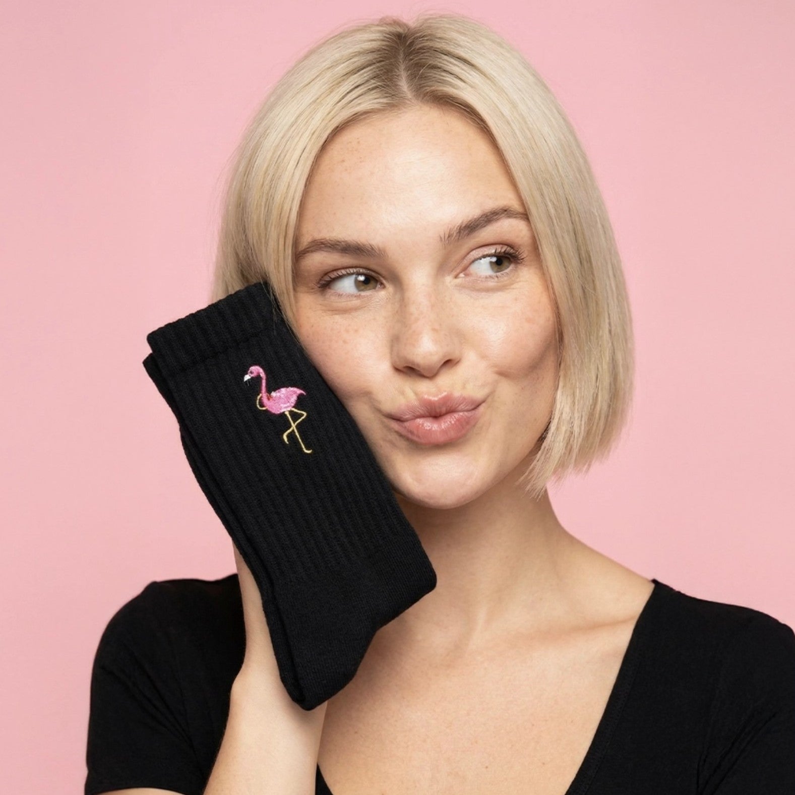Woman holding a black sock with a pink flamingo design against a pink background