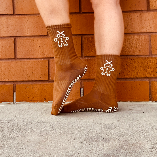 Brown socks with white designs worn by a person against a brick wall.