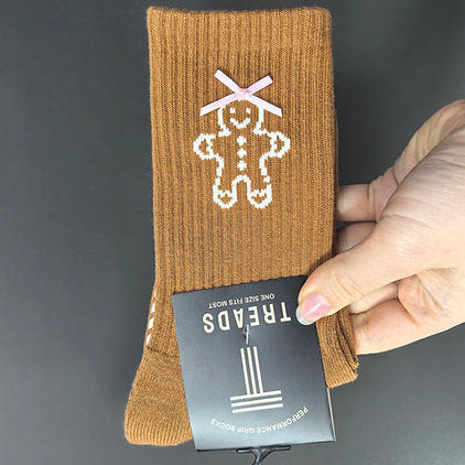 Brown sock with gingerbread man design held by a hand against a dark background