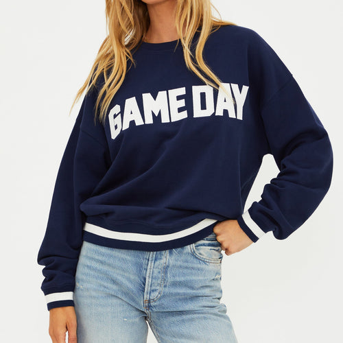 Woman wearing a navy 'GAMEDAY' sweatshirt and light blue jeans on a white background