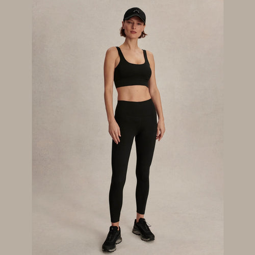 Woman wearing a black sports bra and leggings set on a plain background